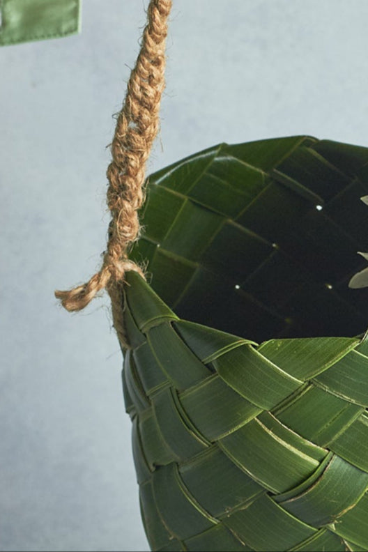 Hand holding a woven leaf basket with a white flower against a light gray background