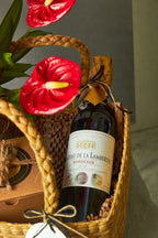 Wine bottle in a woven basket with red anthurium and a box in the background