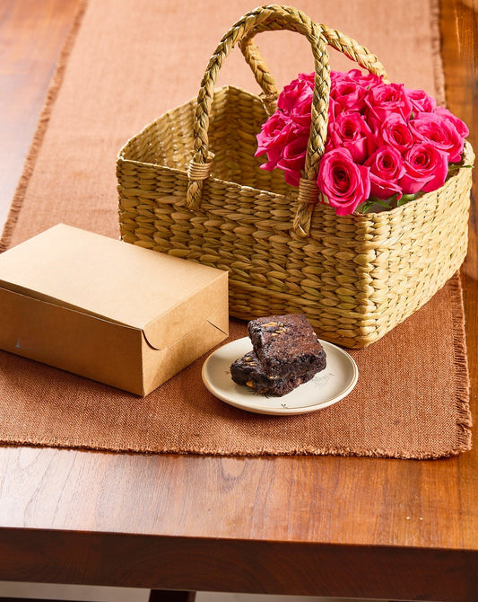 kona basket with pink flowers, brown paper bag, and chocolate cake on a wooden table.