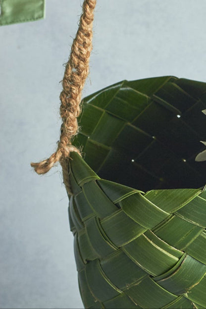 Hand holding a woven leaf basket with a white flower against a light gray background