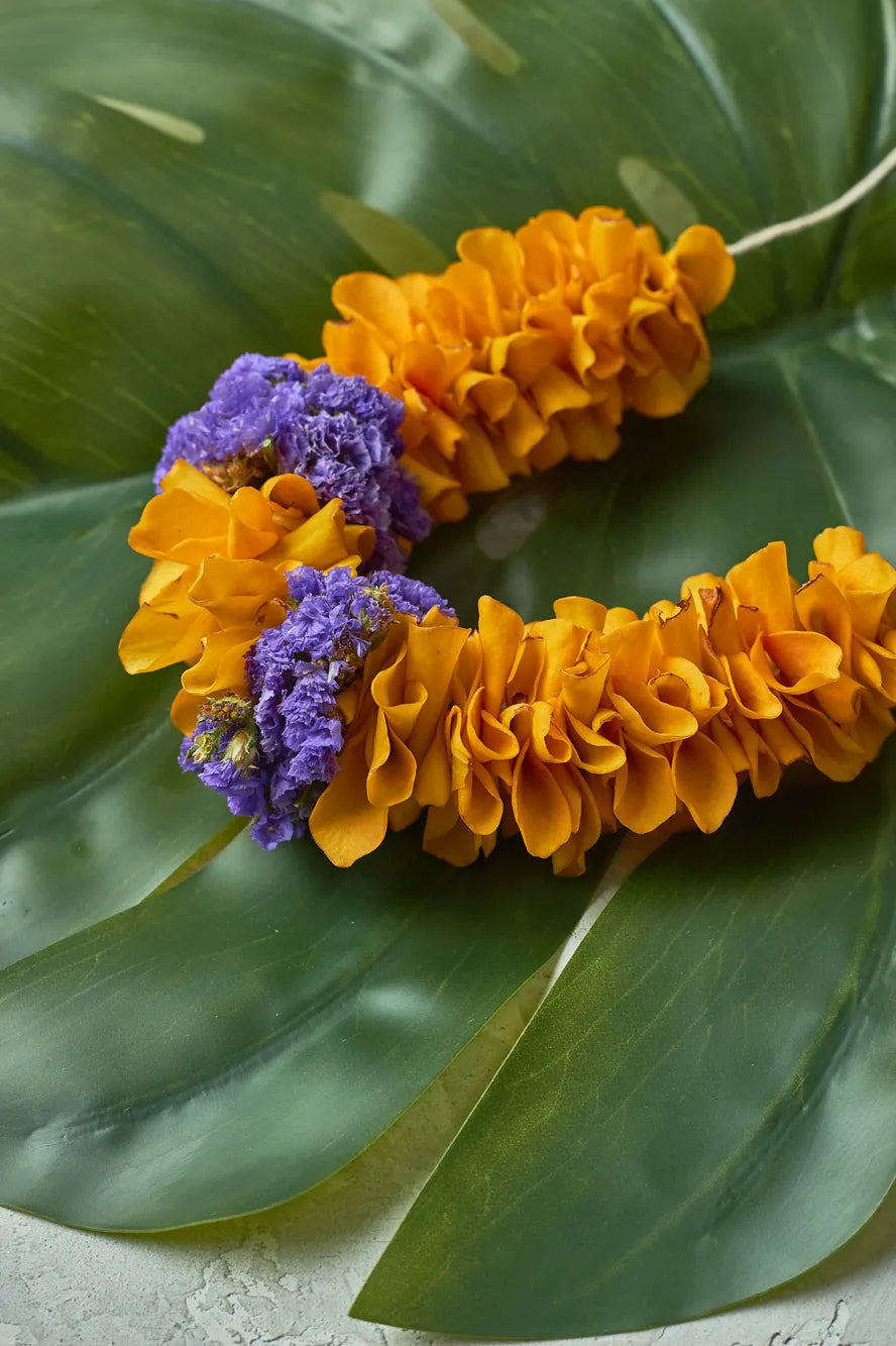 Floral leis with yellow flowers and purple accents on a green leaf background