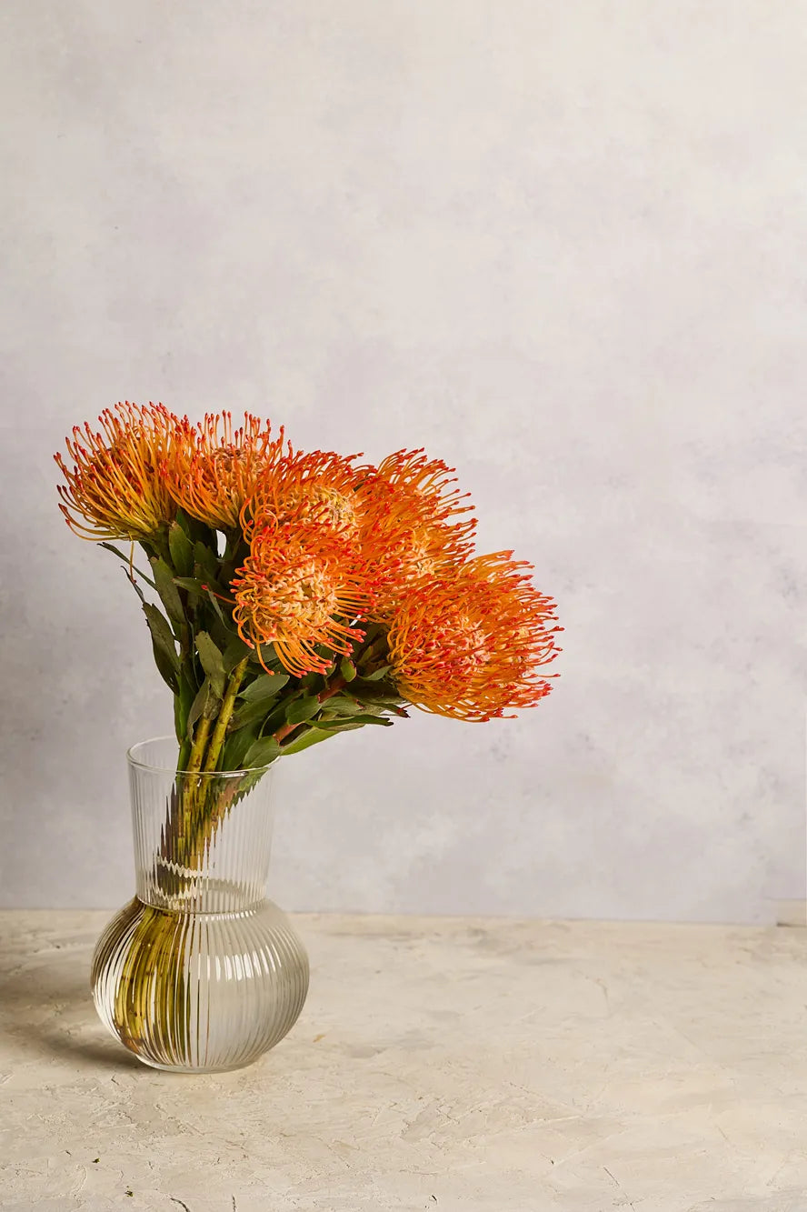 Clear glass vase with orange flowers on a light wooden surface and gray background