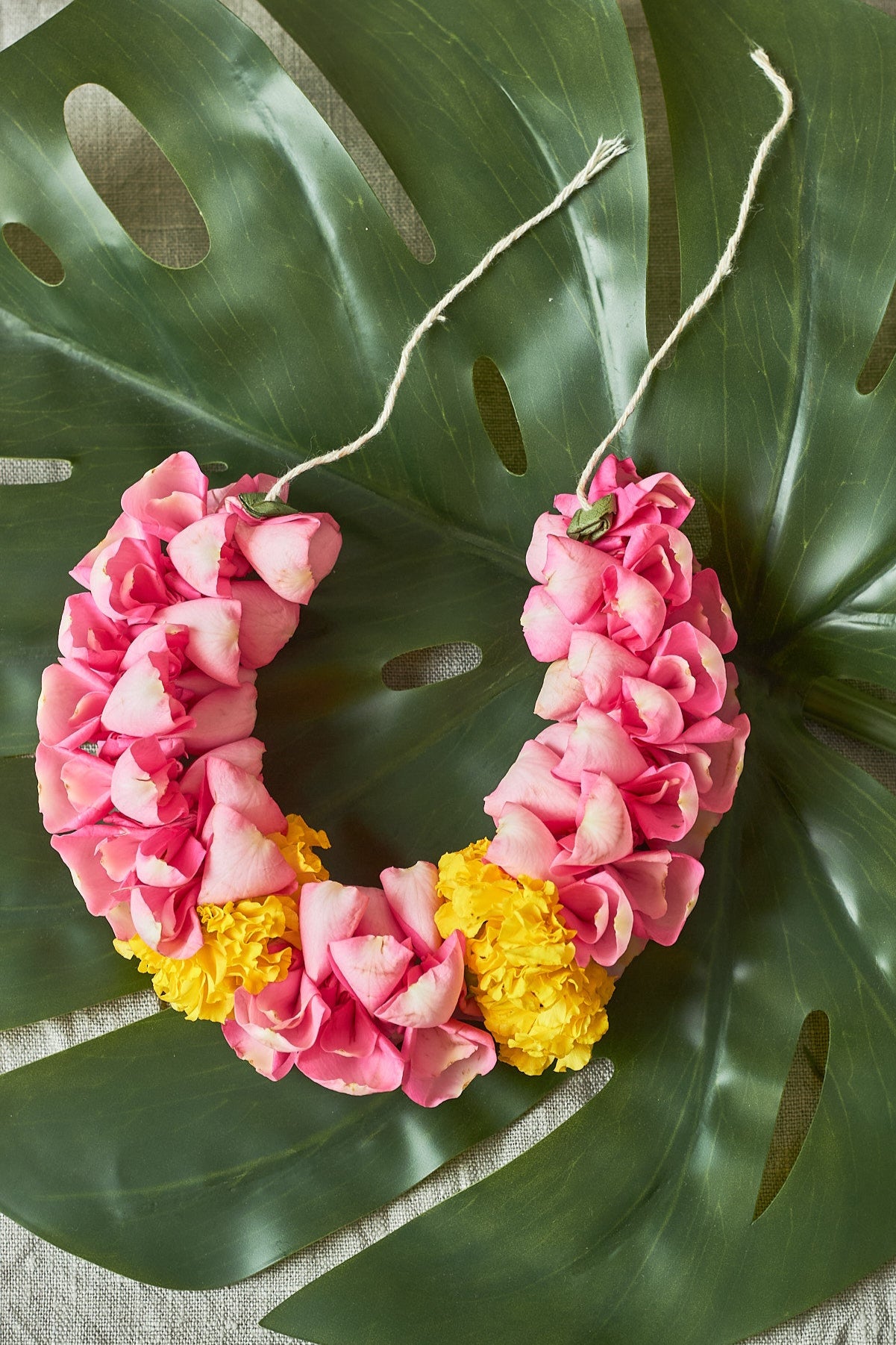 Pink-yellow-gajra-A hair wreath featuring a circle of pink and yellow flowers, with leaves and a string detail.