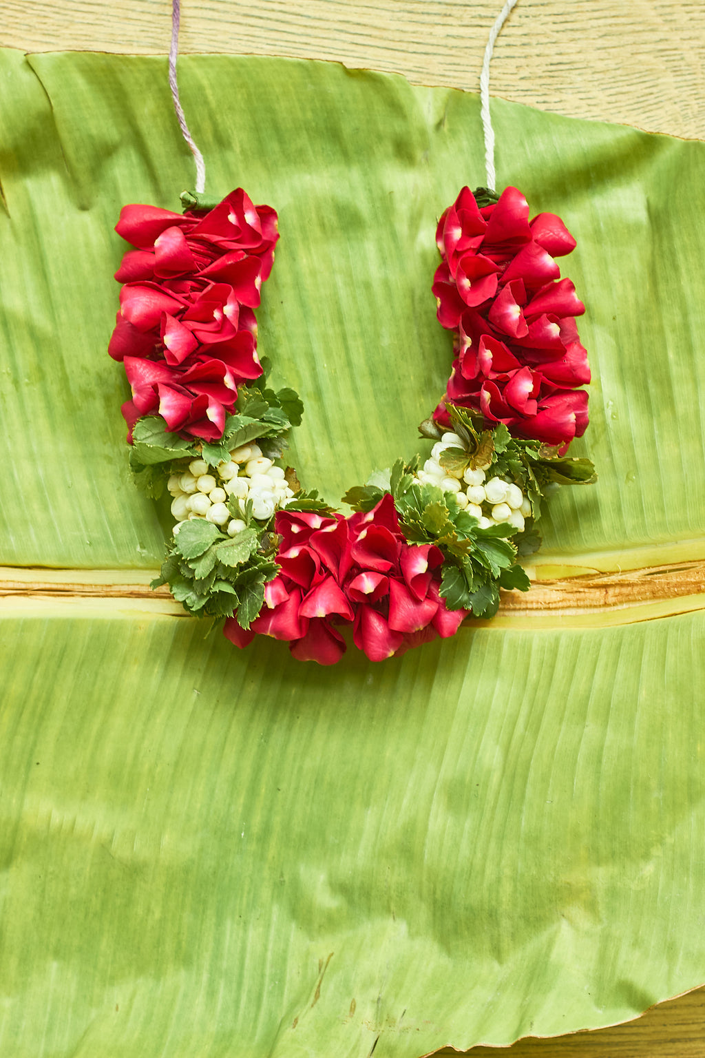 Pyaari-Dulari-Mahua Floral Studio-A wreath of red and green flowers with white accents, designed to be worn at a wedding.
