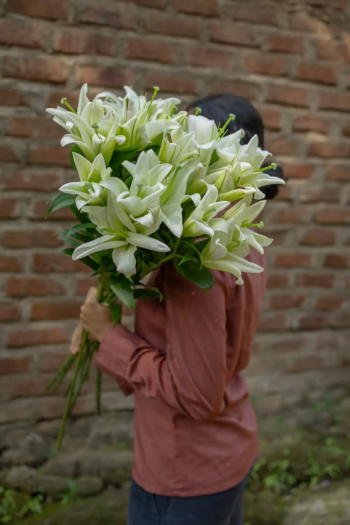 Person holding a large bouquet of white lilies against a brick wall.