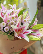 Bouquet of pink and white flowers of lilies and chrysanthemums held by a person outdoors.