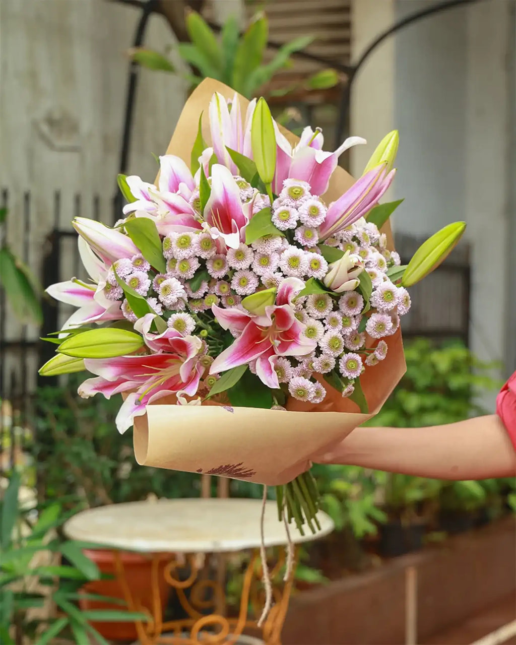 Bouquet of pink and white flowers with green leaves in a paper wrap.