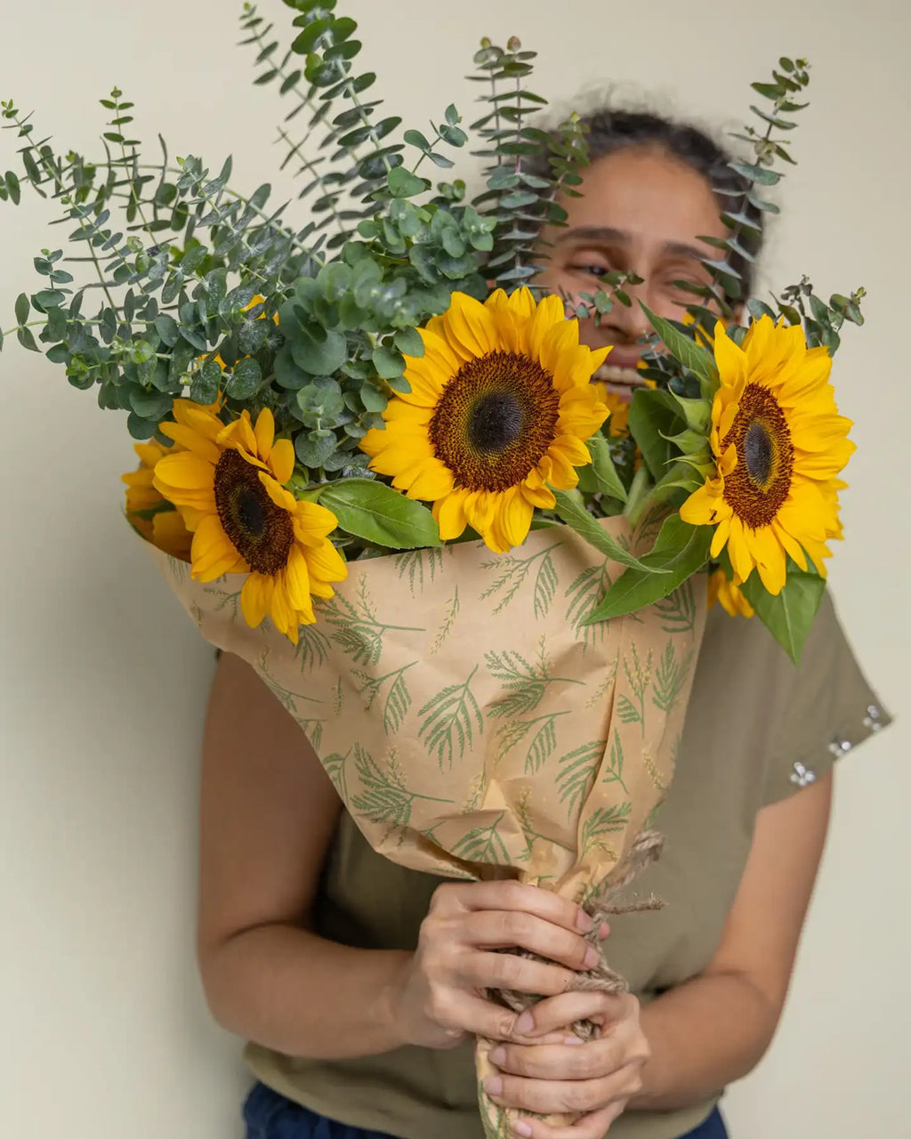 Person holding a bouquet of sunflowers and eucalyptus against a plain background