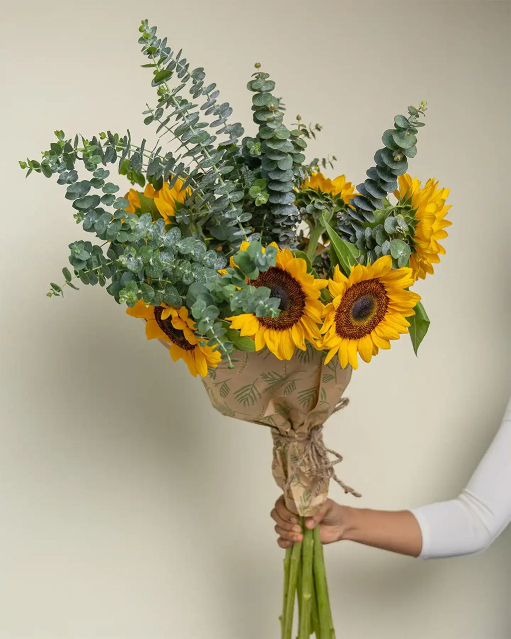 Bouquet of sunflowers and eucalyptus held by a person against a neutral background