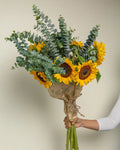 Bouquet of sunflowers and eucalyptus held by a person against a neutral background