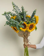 Bouquet of sunflowers and eucalyptus held by a person against a neutral background