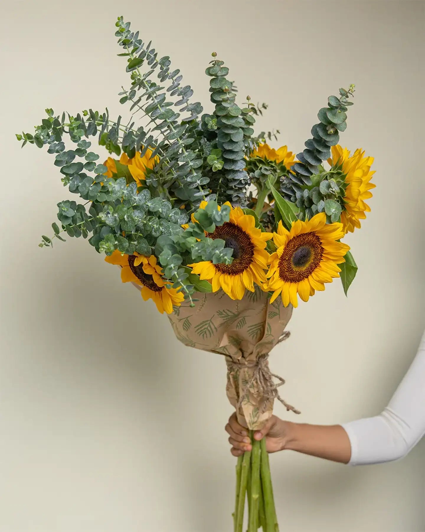 Bouquet of sunflowers and eucalyptus held by a person against a neutral background
