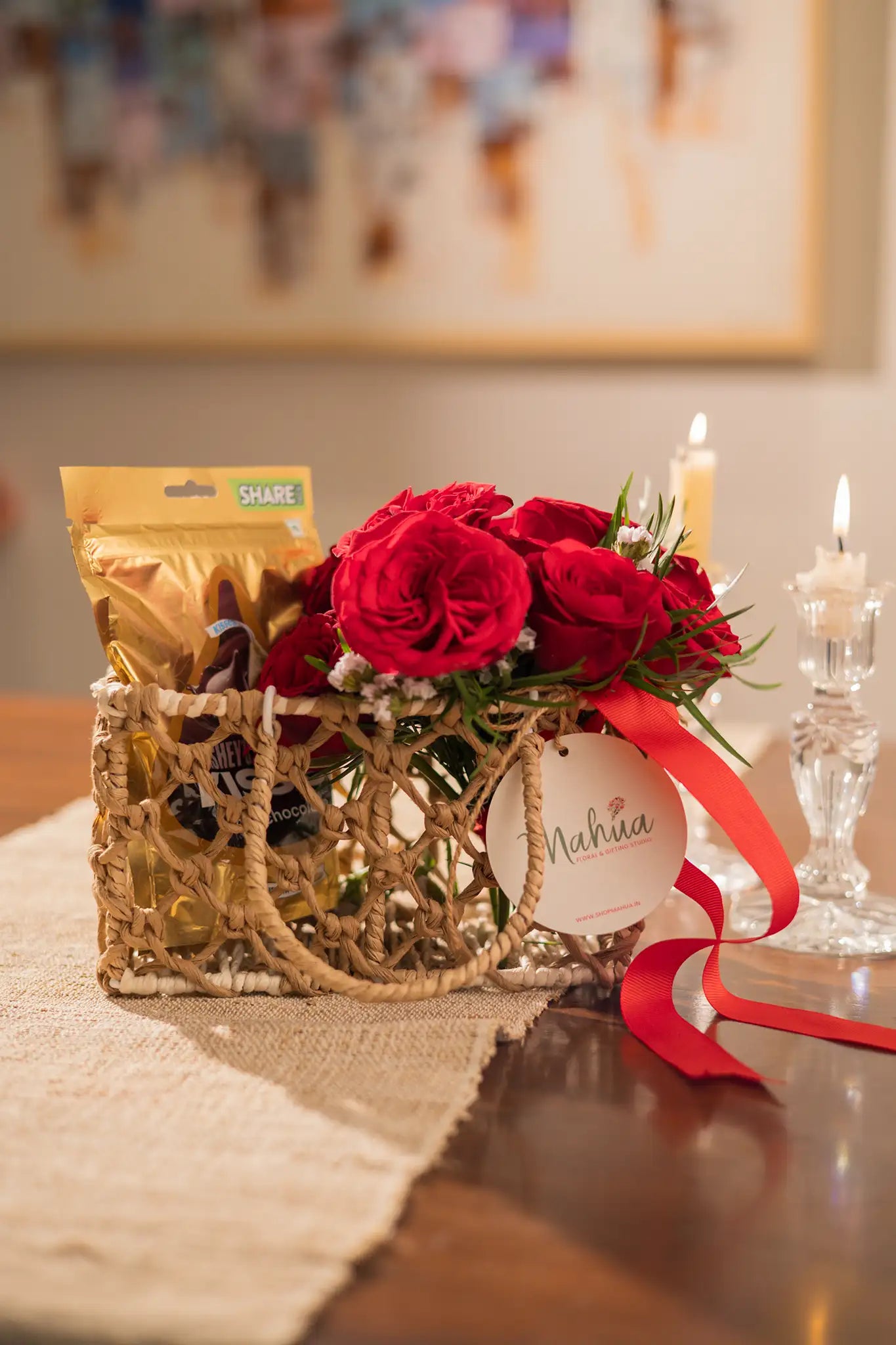 Bouquet of red roses in a decorative bag with candles and a framed picture in the background.