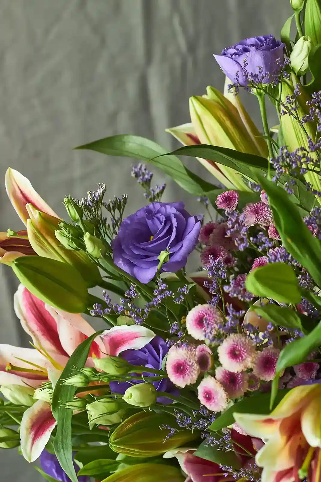 Bouquet of colorful flowers including lilies and eustomas against a neutral background