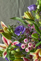 Bouquet of colorful flowers including lilies and eustomas against a neutral background