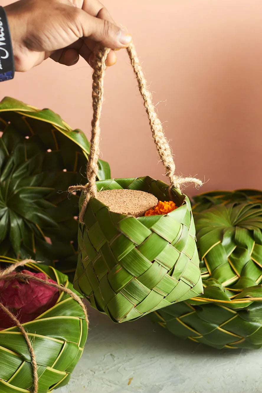 Hand holding a woven green leaf container with a cork lid against a beige background