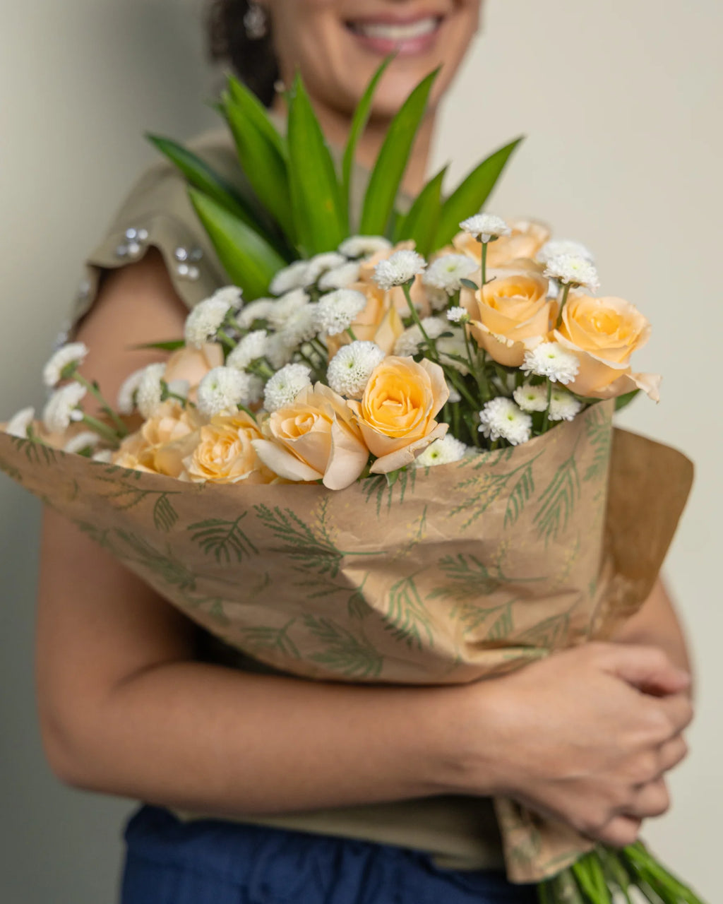 Person holding a bouquet of flowers wrapped in brown paper with green leaf patterns.