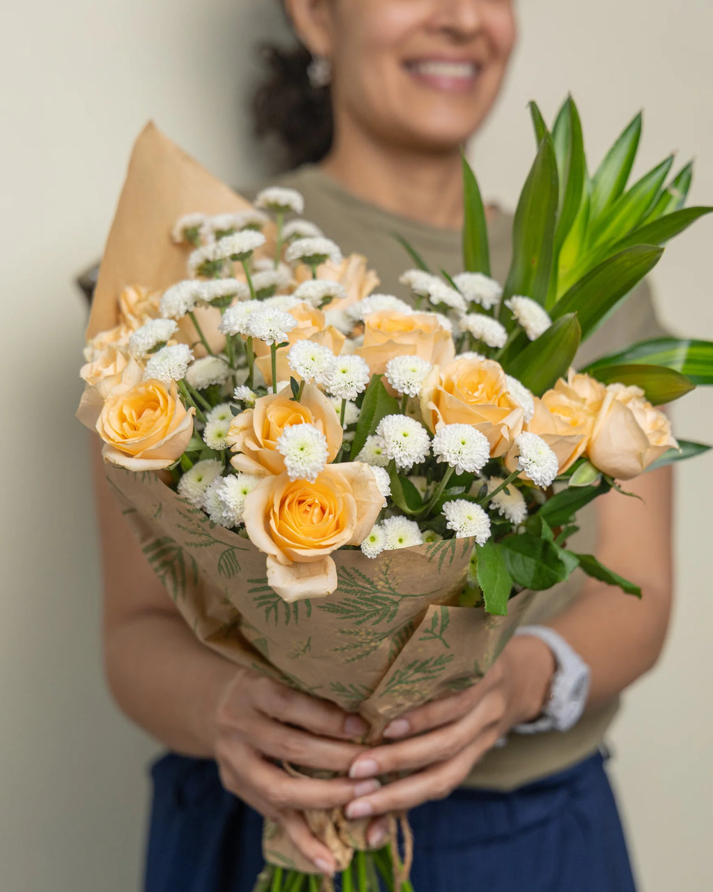 Person holding a bouquet of flowers wrapped in brown paper with greenery.