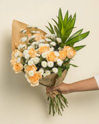 Bouquet of peach and white flowers with greenery held by a person against a beige background