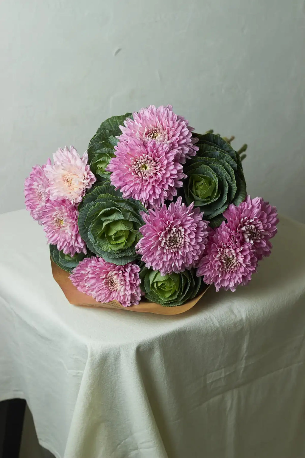 Bouquet of pink flowers and green foliage on a white tablecloth.